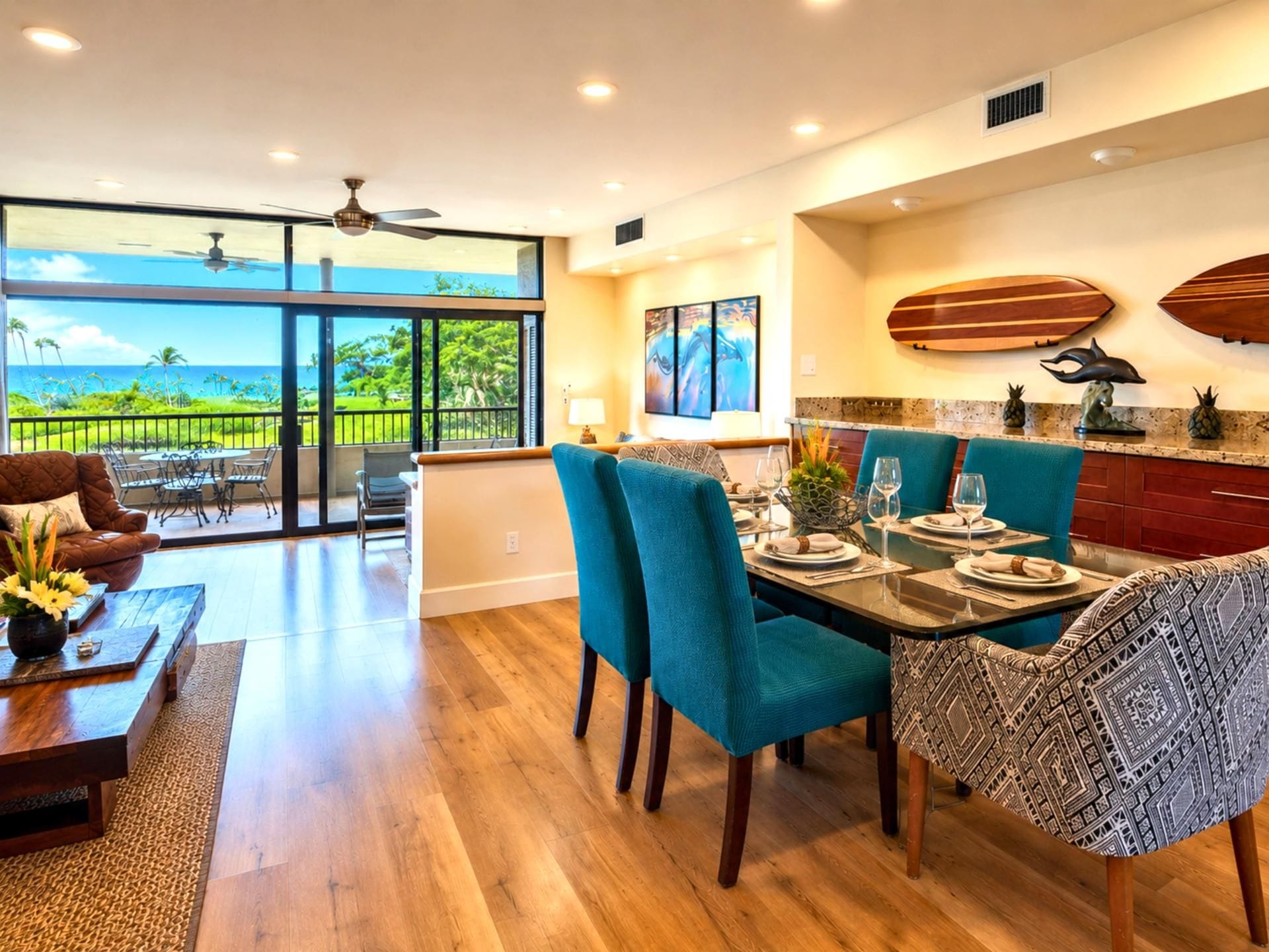 A spacious dining area with a view of the ocean, a ceiling fan, and a kitchen with surfboards on the wall.