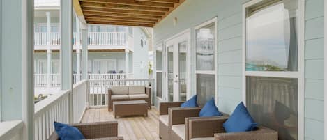 A covered porch with wicker furniture and a view of a residential building.