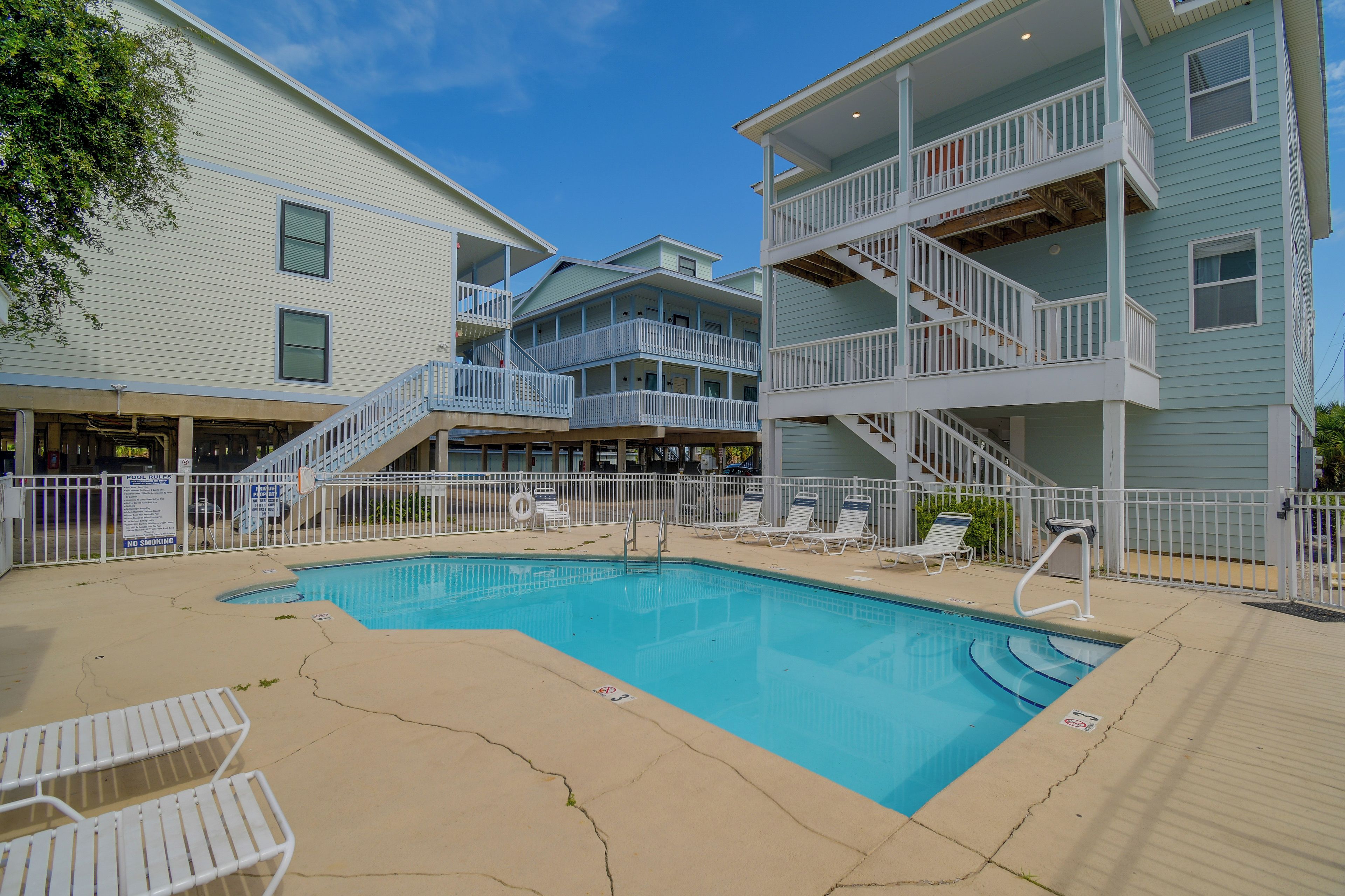 A pool area with a clear blue pool, white lounge chairs, and a staircase leading to a multi-level building.