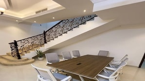Een vergaderzaal met een grote tafel, witte stoelen en een trap met decoratieve leuningen.