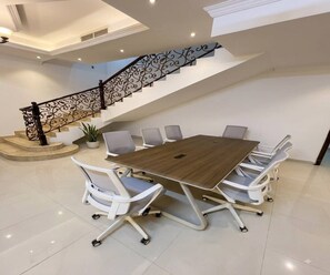 Un salón de conferencias con una gran mesa, sillas blancas y una escalera con barandales ornamentados.