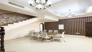 Una sala de conferències espaiosa amb una taula llarga i cadires, una escala amb baranes ornamentals i un llum modern.