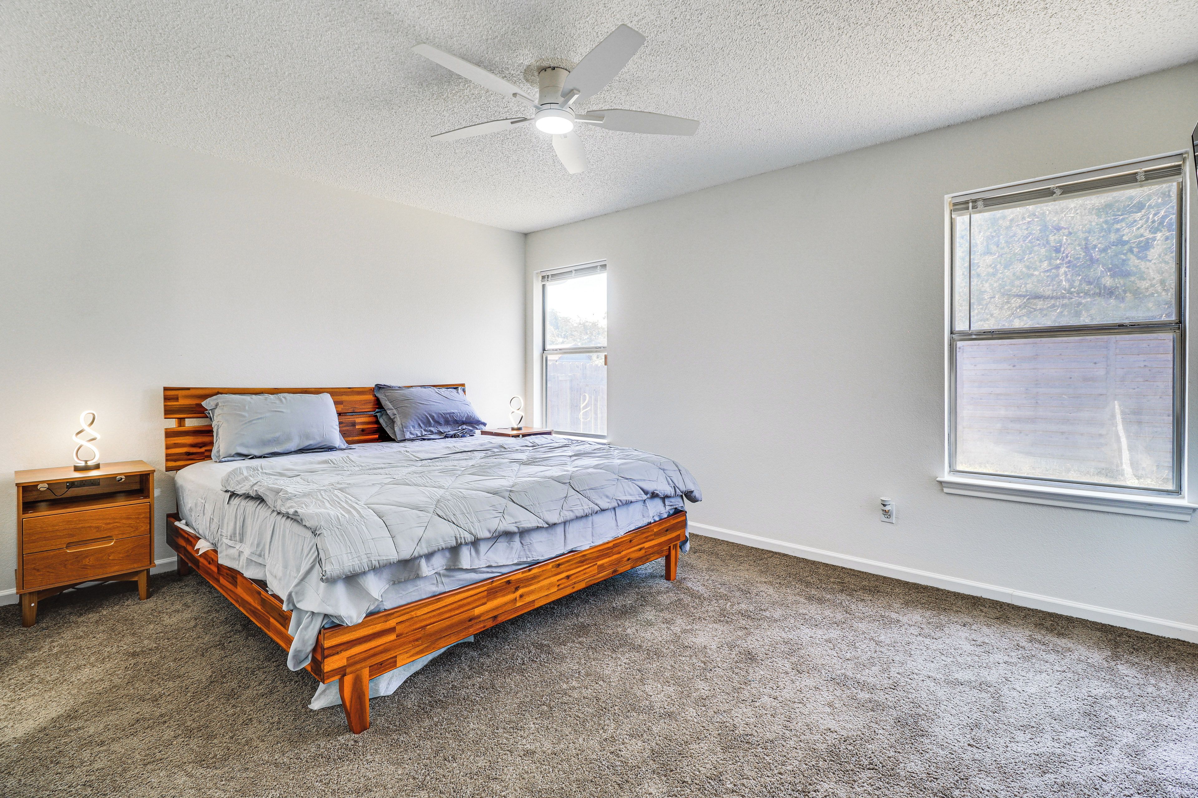 A bedroom with a wooden bed, a nightstand, a ceiling fan, and a large window.