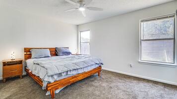 A bedroom with a wooden bed, a nightstand, a ceiling fan, and a large window.