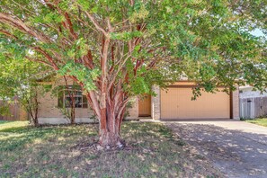 Una propiedad residencial con garaje, un árbol en el frente y una casa de ladrillo.