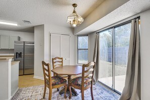 Un comedor con una mesa y sillas de madera, una cocina con refrigerador y un ventanal con cortinas.