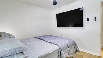 Ein Schlafzimmer mit einem Einzelbett, einem flachbildfernseher an der Wand und einem Deckenventilator.