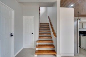 A staircase with wooden steps leading to a landing, white walls, and a kitchen area with a refrigerator.