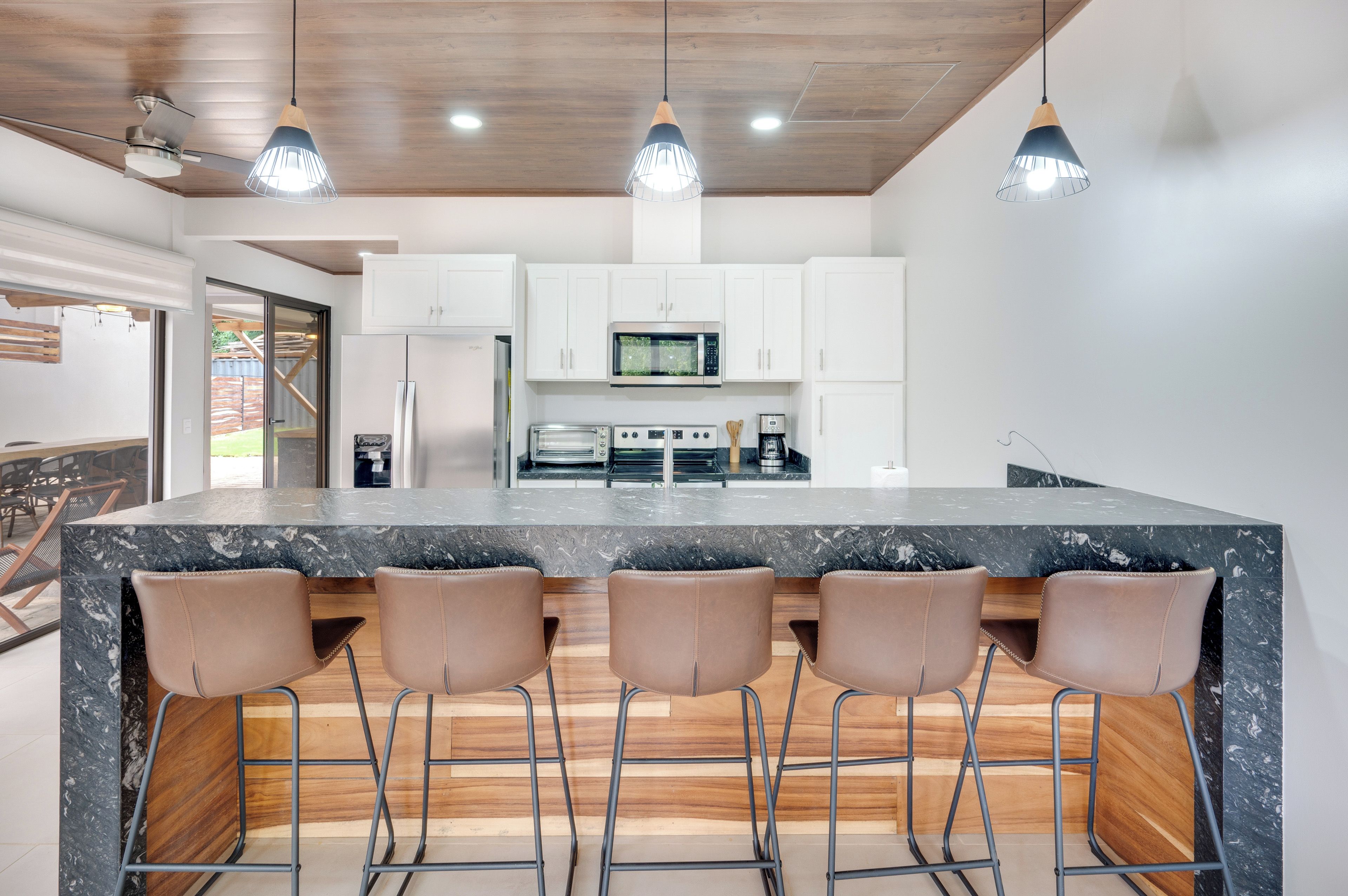 Una cocina moderna con una isla central, taburetes de bar, armarios blancos e iluminación colgante.