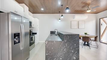 Cocina moderna con una isla de mármol, electrodomésticos de acero inoxidable, iluminación colgante y ventilador de techo.