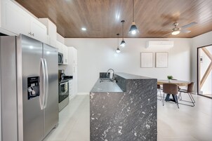 Cocina moderna con una isla de mármol, electrodomésticos de acero inoxidable, iluminación colgante y ventilador de techo.