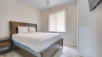 Un dormitorio con cama, mesita de noche, cabecera de madera, ventilador de techo y ventana con persianas.