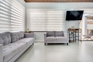 A modern living room with two sofas, a flat-screen TV, and a wooden ceiling.