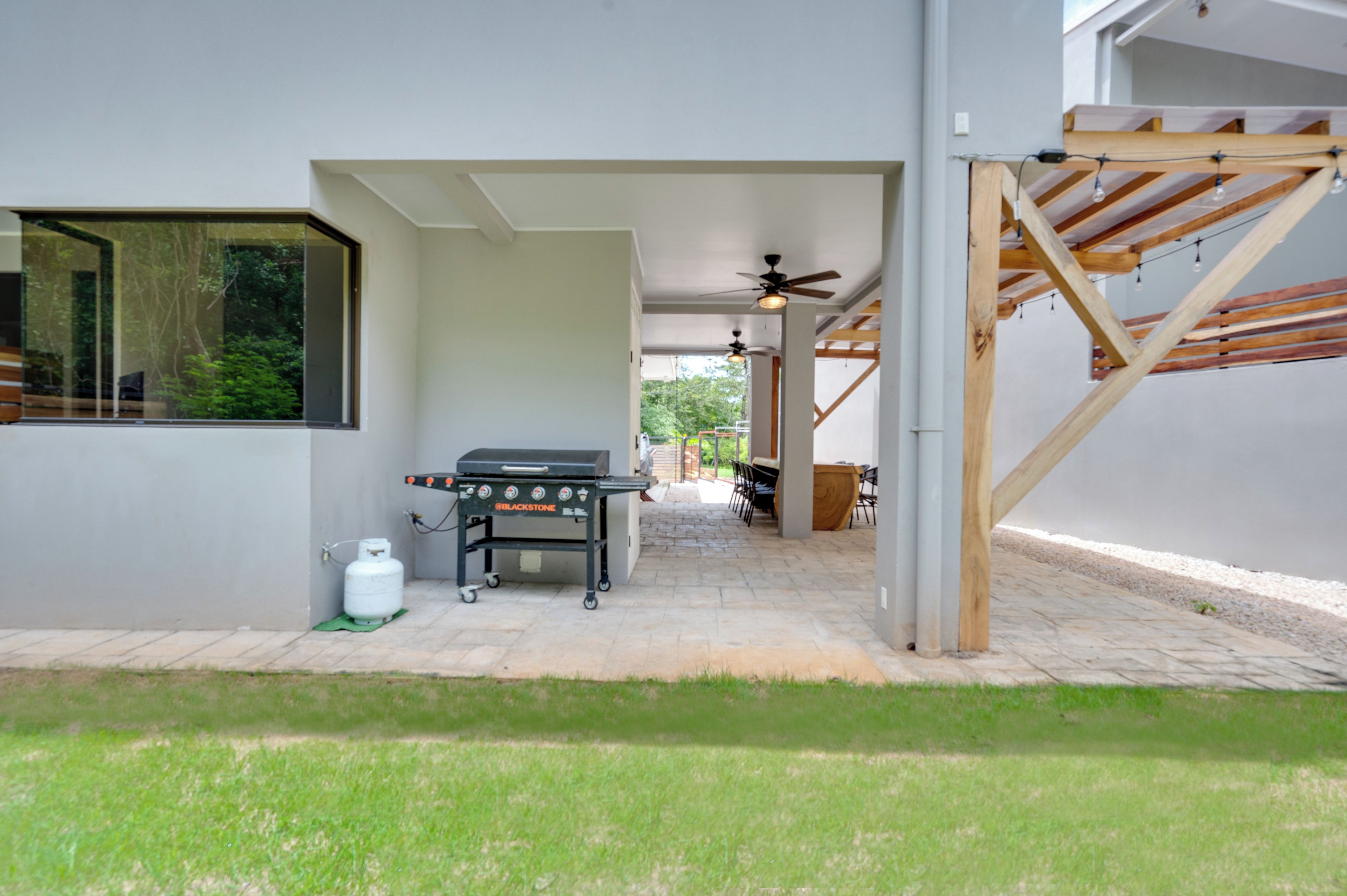 Un patio con una parrilla, un ventilador de techo y vista a un jardín.
