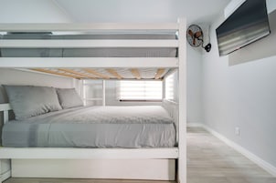 Dormitorio con literas, ventana, ventilador de pared y toma de corriente.