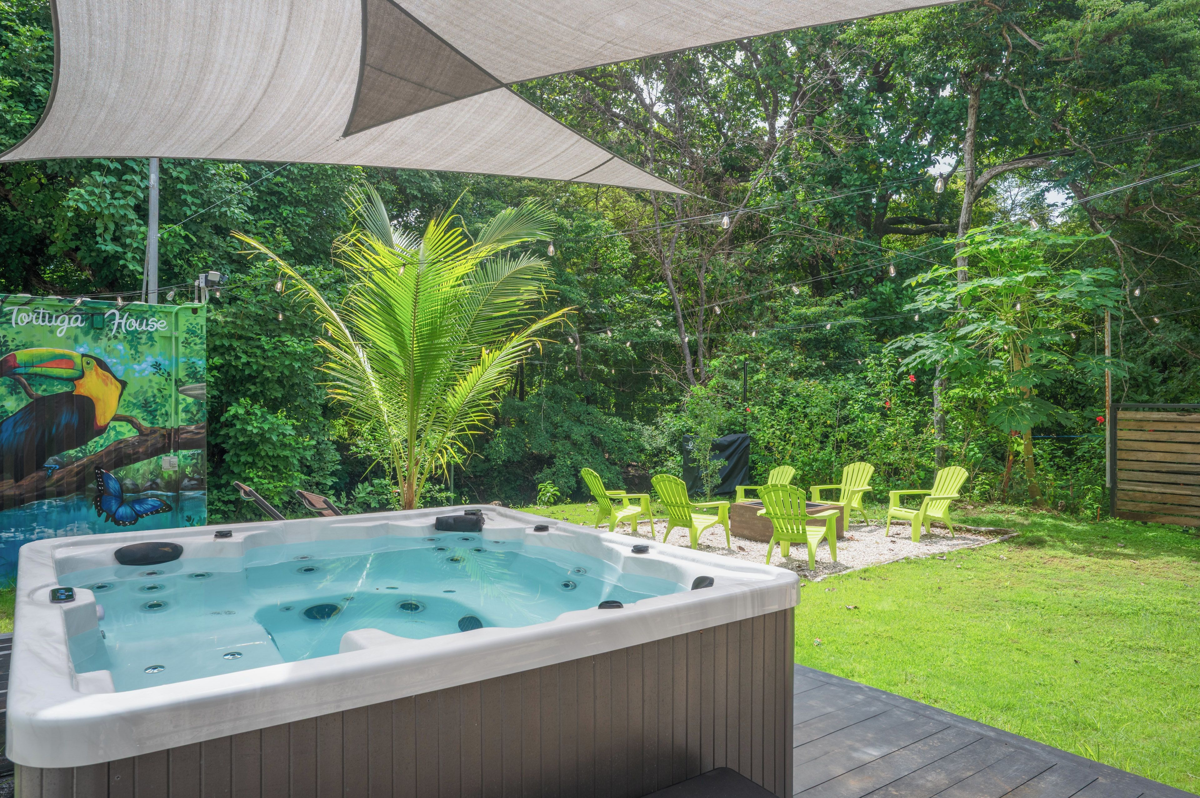 A hot tub with a wooden deck, surrounded by greenery and a mural of a toucan.