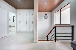 Un interior moderno con una escalera, armarios blancos y un ventanal amplio.