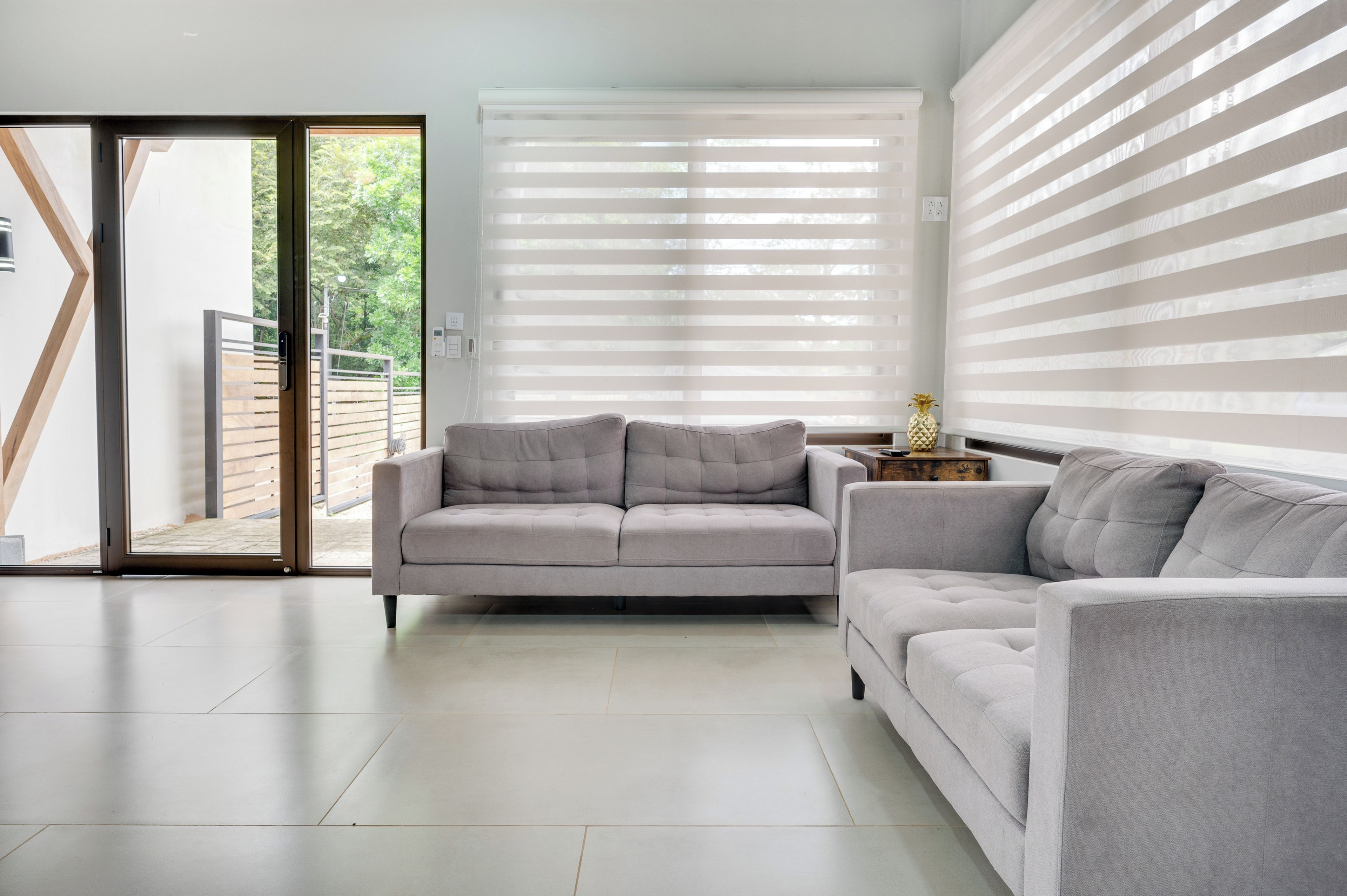 Una sala moderna con un sofá gris, un vidrio corredero que da a un espacio exterior y una pared con persianas horizontales.
