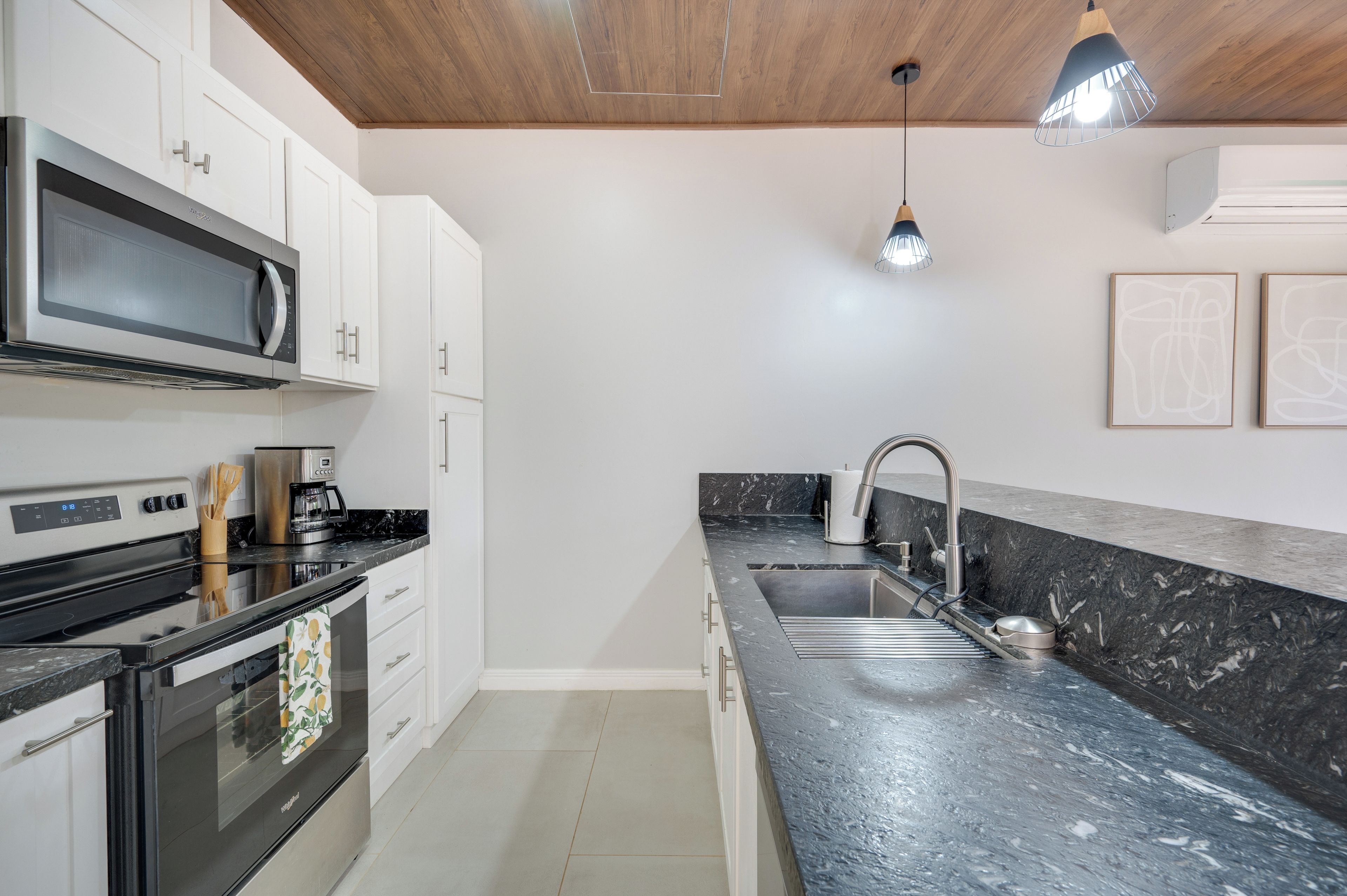 A modern kitchen with white cabinets, a black countertop, stainless steel appliances, and a marble backsplash.