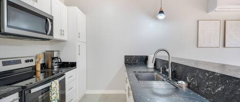 A modern kitchen with white cabinets, a black countertop, stainless steel appliances, and a marble backsplash.