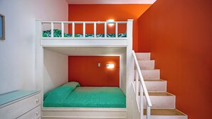 Un letto a castello con materasso verde, una cassettiera bianca e una scala su una parete arancione.
