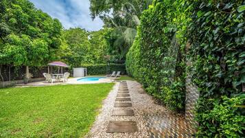 A backyard with a swimming pool, a patio with chairs, and a stone pathway leading to a door.