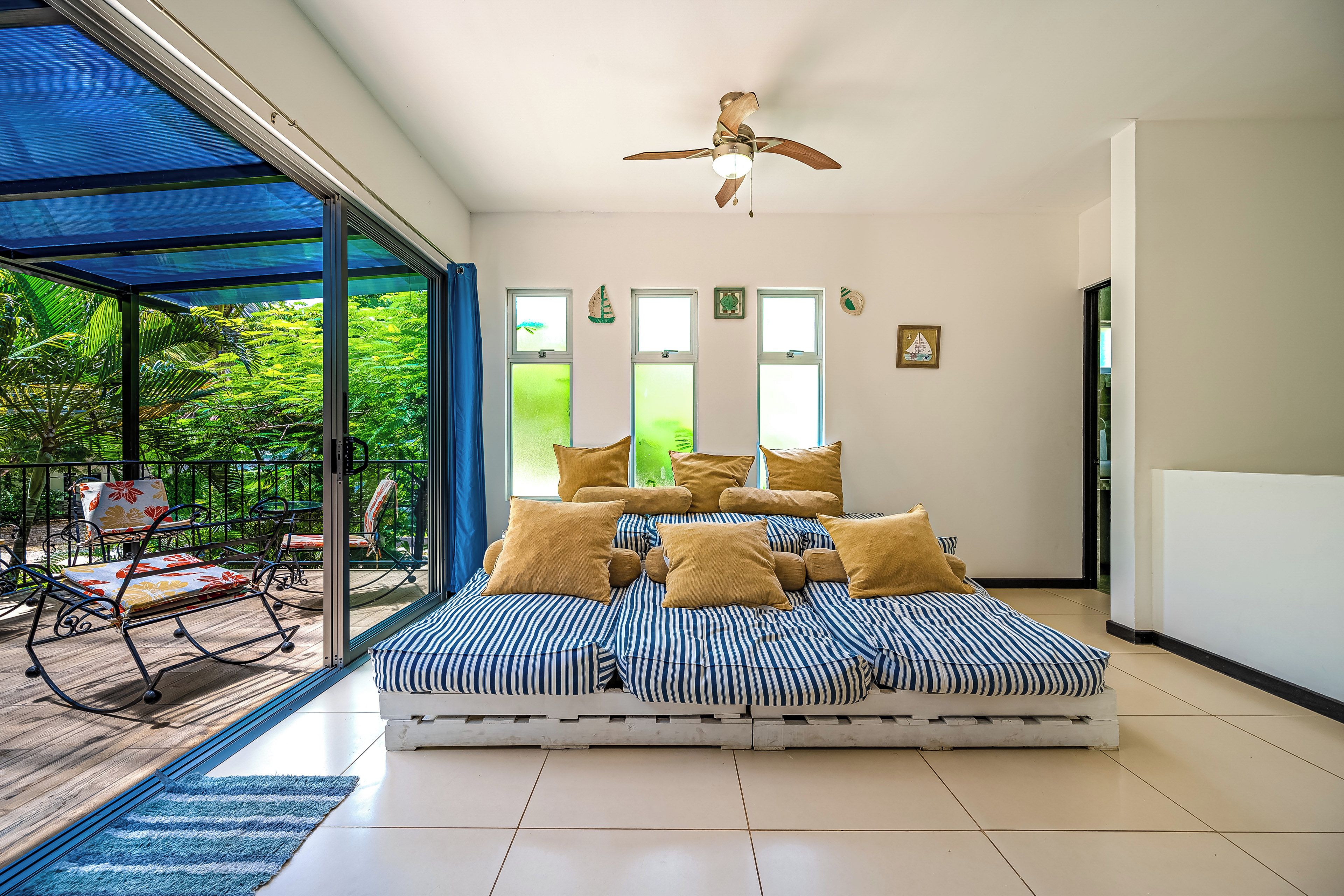 A spacious room with a large bed, a ceiling fan, and a view of a lush garden through large windows.
