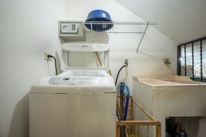 A compact, white washing machine with a control panel, a blue water tank, and a metal rack above it.