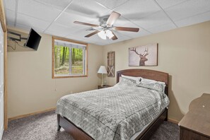 A bedroom with a bed, a ceiling fan, a window with a view of trees, a mounted TV, and a painting of an elk. - Epic Lake Harmony Group Getaway! (Lake Harmony)