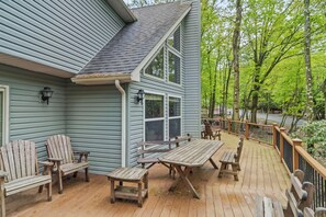 A wooden deck with outdoor furniture, a covered area with a table and chairs, and a view of a forested area. - Epic Lake Harmony Group Getaway! (Lake Harmony)