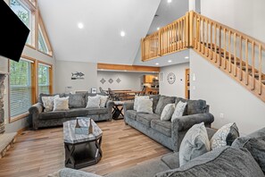 A spacious living area with a high ceiling, a wooden staircase, and a view of the outdoors. - The Ultimate Lake Harmony Group Getaway Awaits! (Lake Harmony)