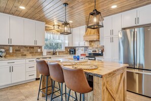 A modern kitchen with white cabinets, a large island with stools, stainless steel appliances, and wooden ceiling beams.
