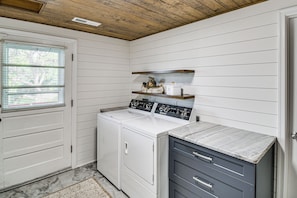 A laundry room with a front-loading washer and dryer, a small shelf with decorative items, and a marble countertop.