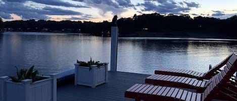 Une terrasse en bois, agrémentée de bancs et de jardinières, qui offre une vue sur un lac paisible au crépuscule.