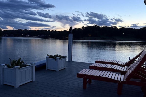 A wooden deck with benches and planters overlooking a calm lake at dusk.