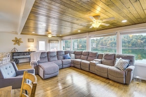 A spacious living room with a large sectional sofa, wooden flooring, and a view of a lake through large windows.