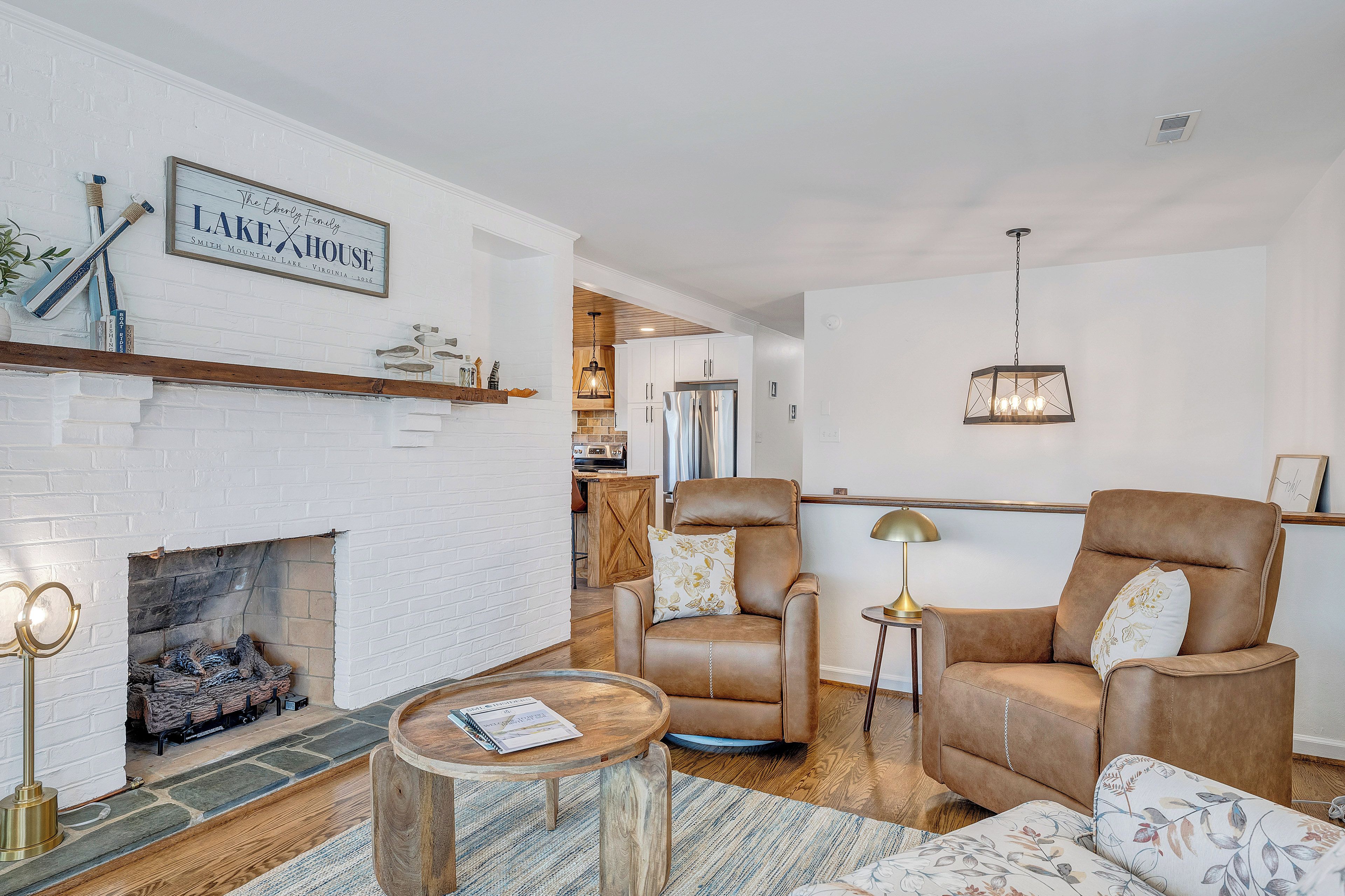 A living room with a fireplace, leather armchairs, a coffee table, and a hanging light fixture.