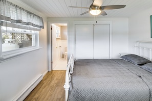 A bedroom with a bed, a ceiling fan, a window with curtains, and a door leading to a bathroom.
