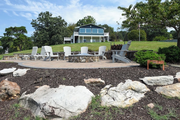 A house with a deck, outdoor seating, and a stone fire pit.