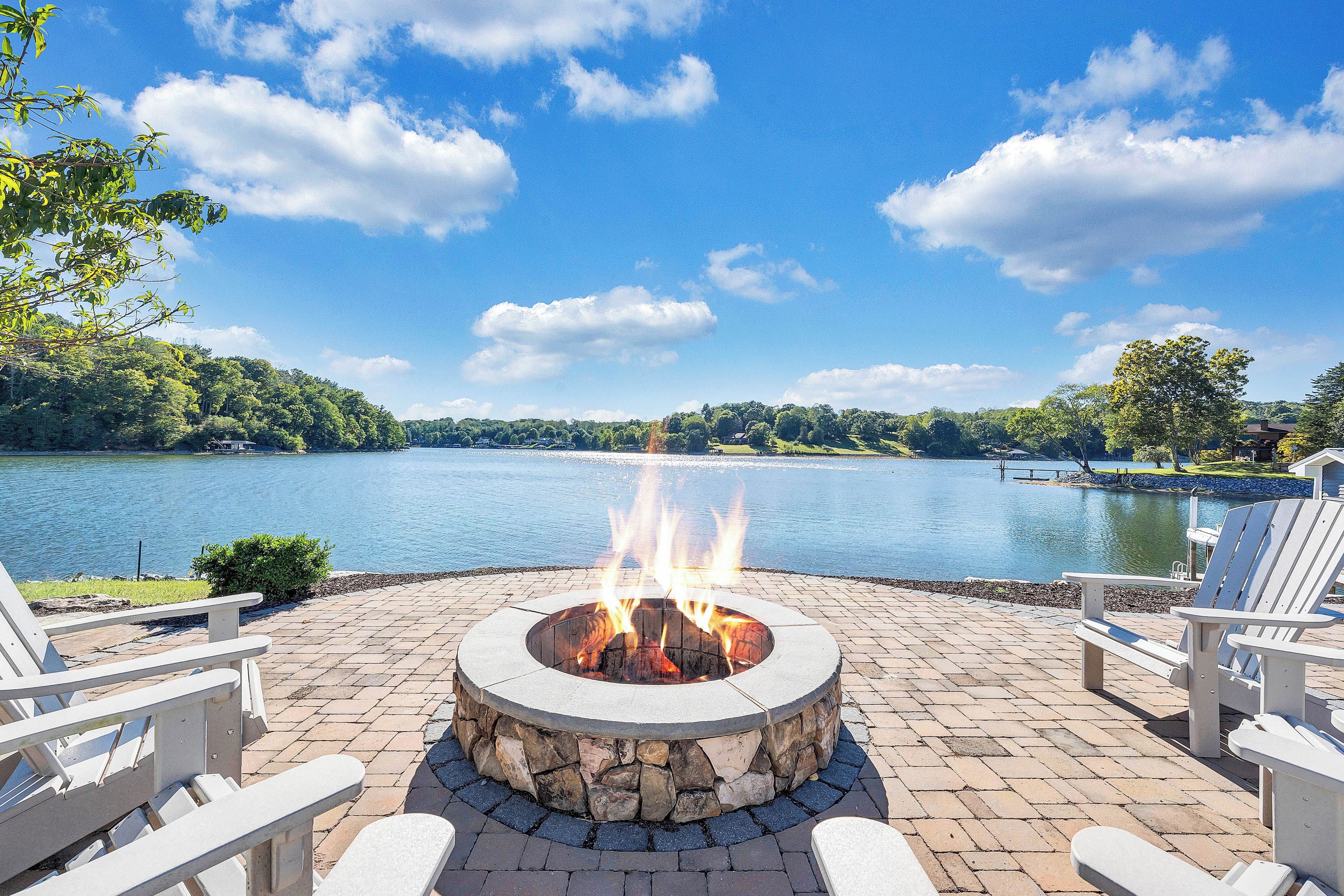 A fire pit with a lake view, surrounded by white chairs.