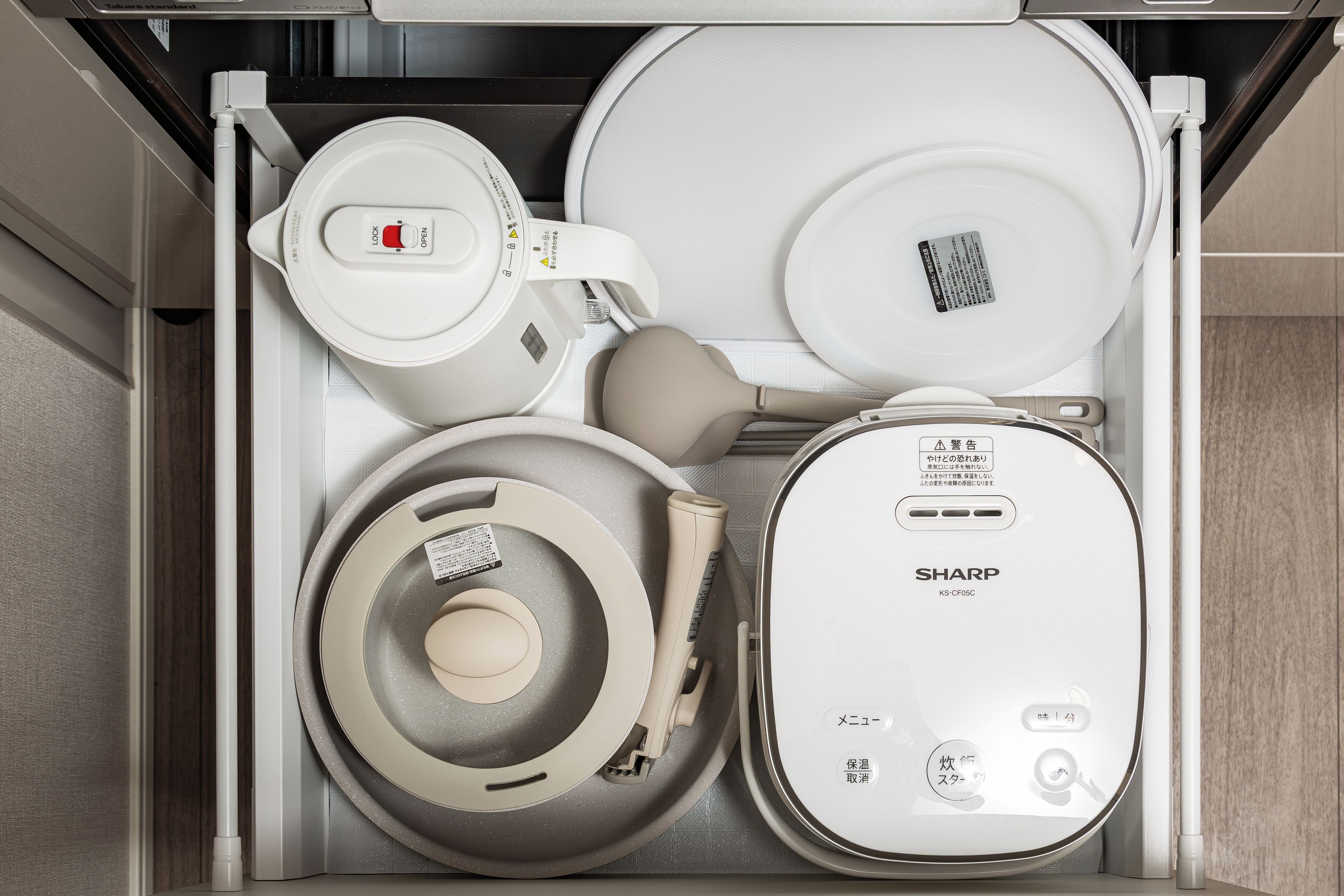 A kitchen drawer with various appliances including a rice cooker, a water boiler, a rice pot, and a Sharp rice cooker.