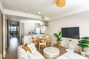 Una sala de estar moderna con sofá, mesa de comedor, sillas, una cocina equipada y un televisor montado en la pared.