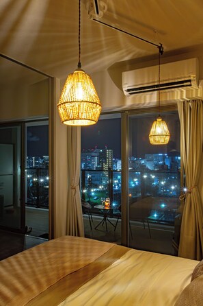 Una habitación de hotel con cama, una mesa y vista a un paisaje urbano nocturno.
