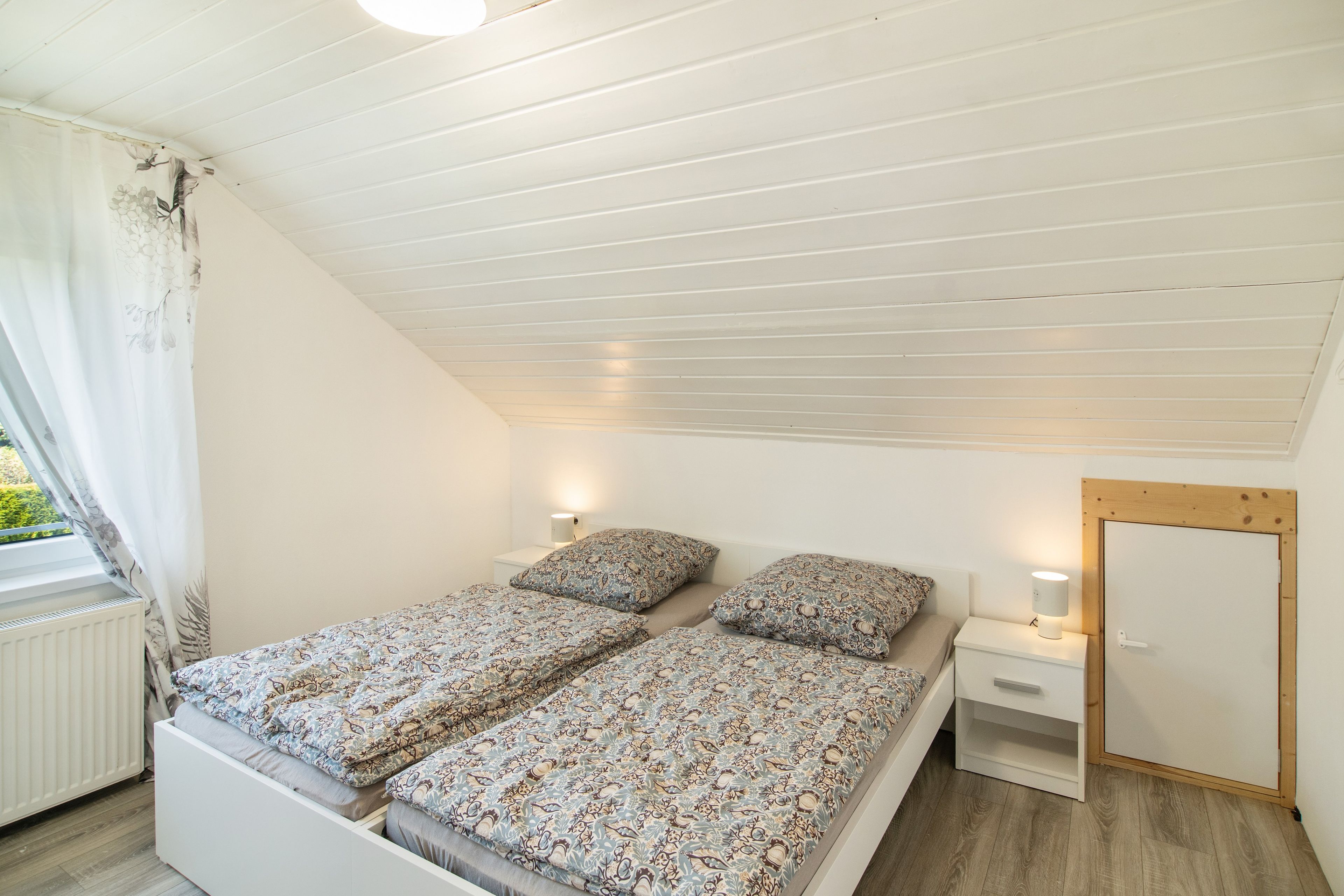 Ein Schlafzimmer mit einem Bett, Nachttischen, einem Spiegel und einem Fenster mit Vorhängen.