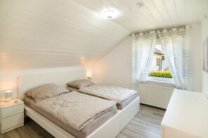 Et soveværelse med skrå vægge, en seng med gavl, sengeborde med lamper, et vindue med gardiner og en radiator.