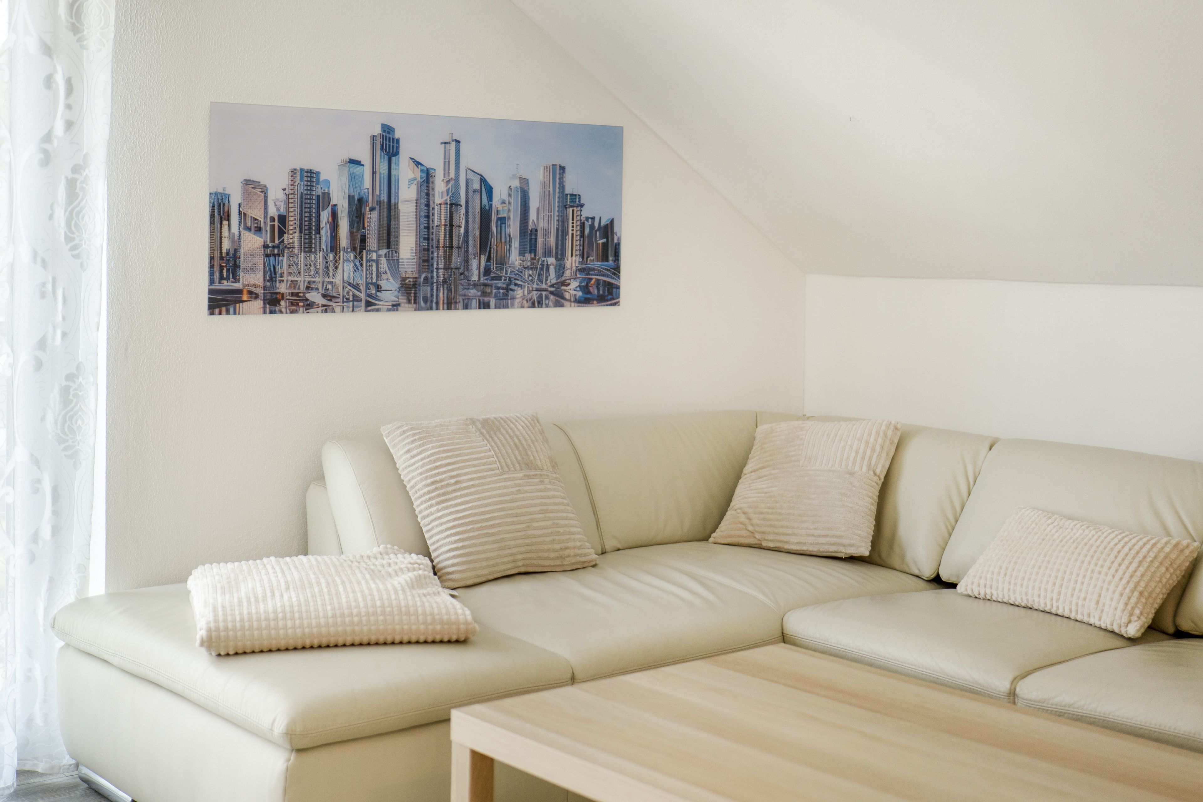 A modern living room with a sectional sofa, a coffee table, and a cityscape painting on the wall.