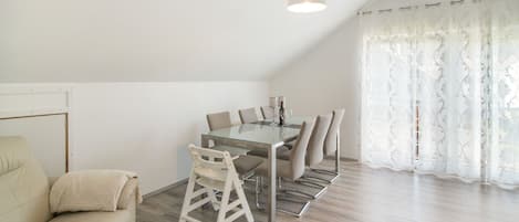 A modern living room with a sofa, a dining table with chairs, and a ceiling light fixture.