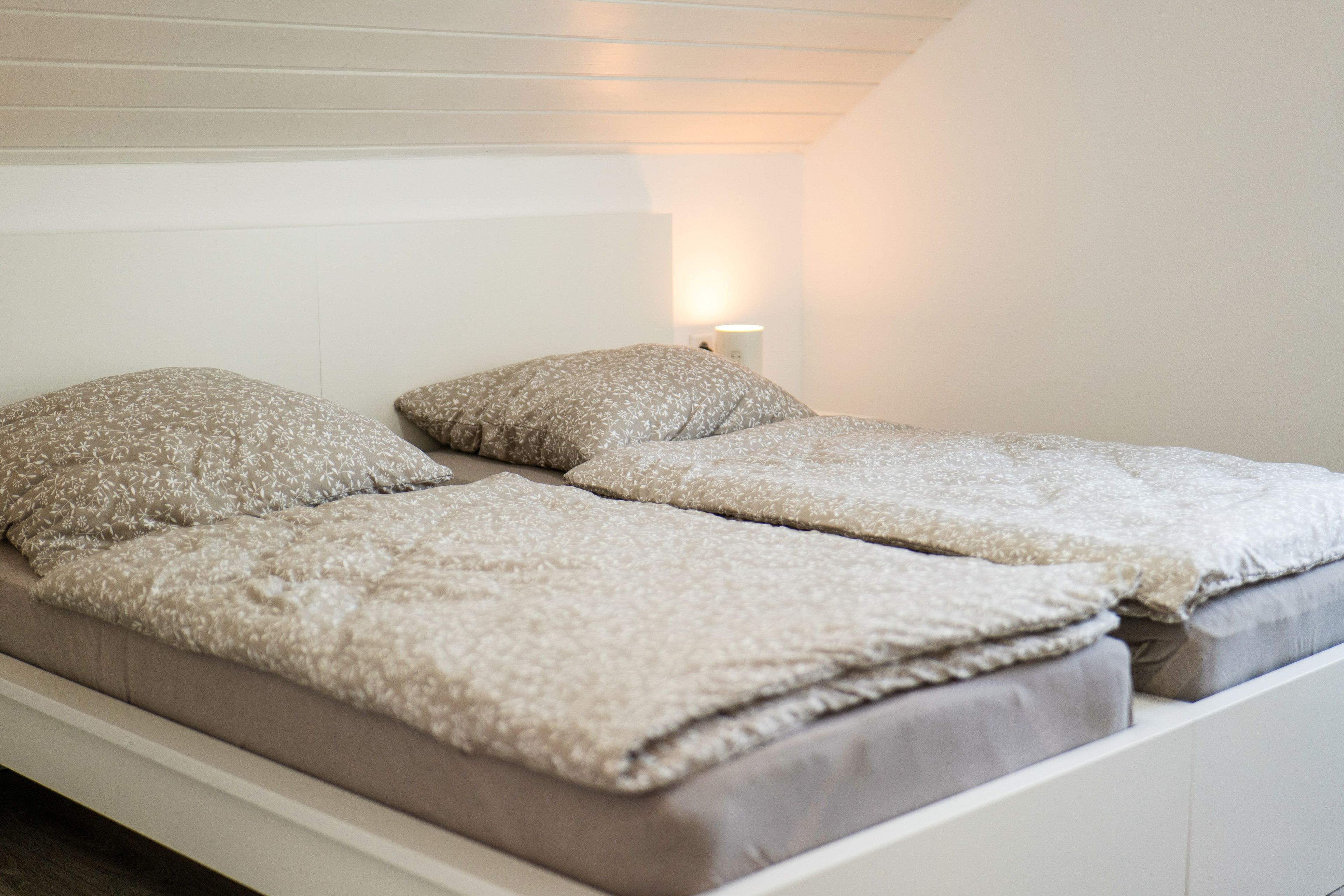 Una cama individual con colchón blanco y dos almohadas, una lámpara de noche y una pared blanca.