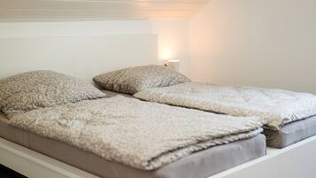 Una cama individual con colchón blanco y dos almohadas, una lámpara de noche y una pared blanca.