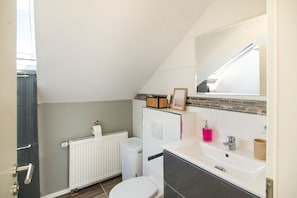 Et lille badeværelse med toilet, hvid vask og et spejl over vasken.